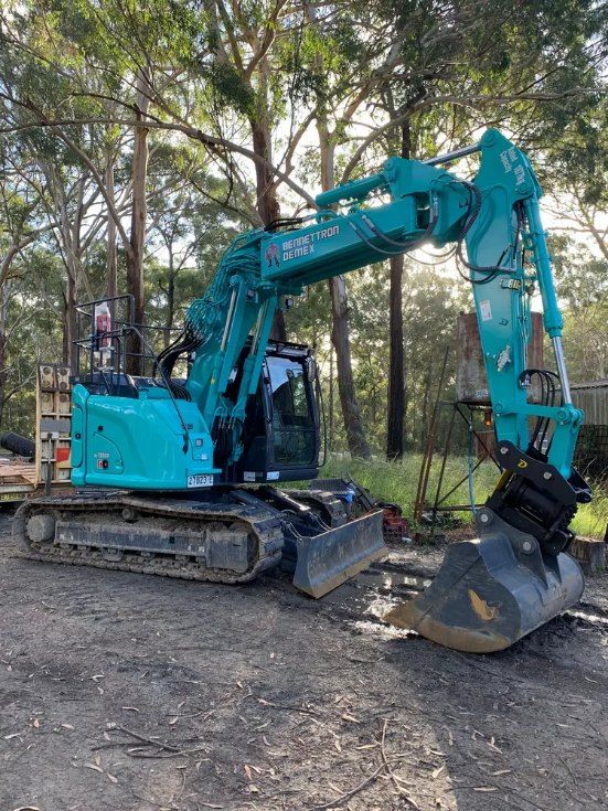 A large blue digger is parked on side of gravel road — Bennettron Demex in Corindi Beach, NSW