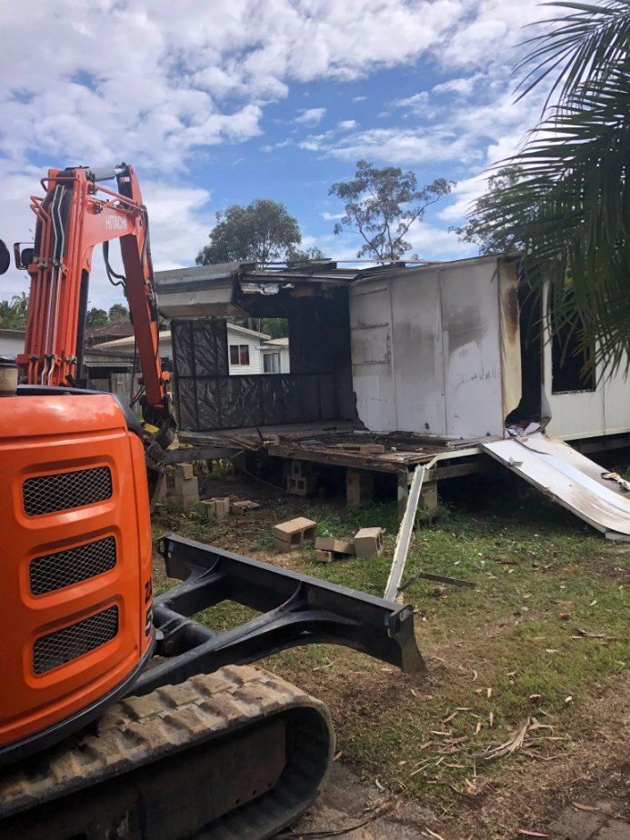 A Small Orange Excavator is Standing in Front of a House Being Demolished — Bennettron Demex in Kyogle, NSW