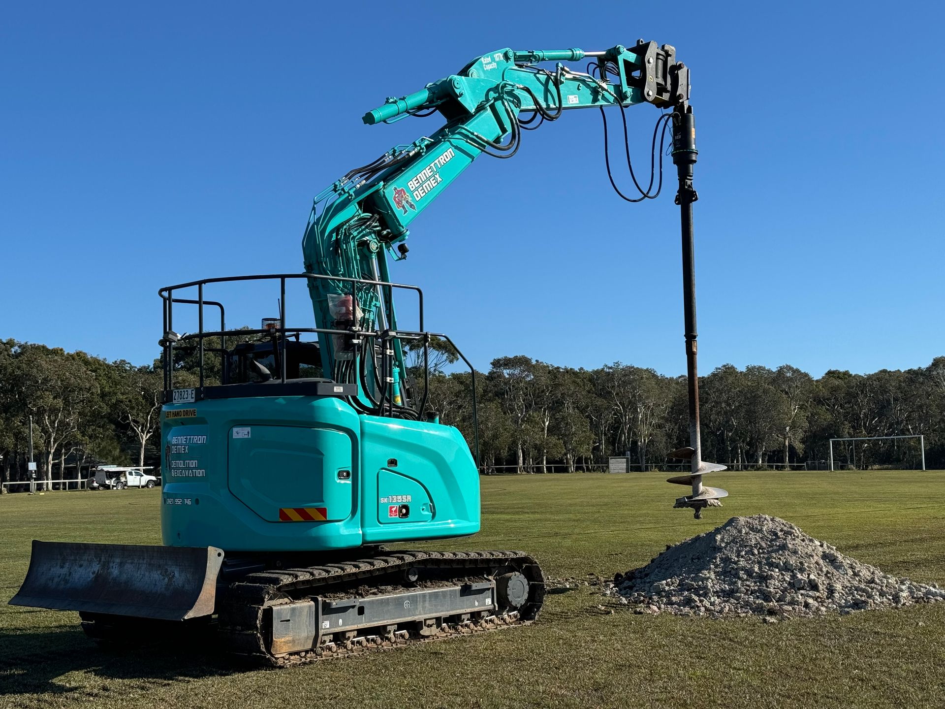 A large blue digger has a large drill and is drilling a field of grass — Bennettron Demex in Corindi Beach, NSW