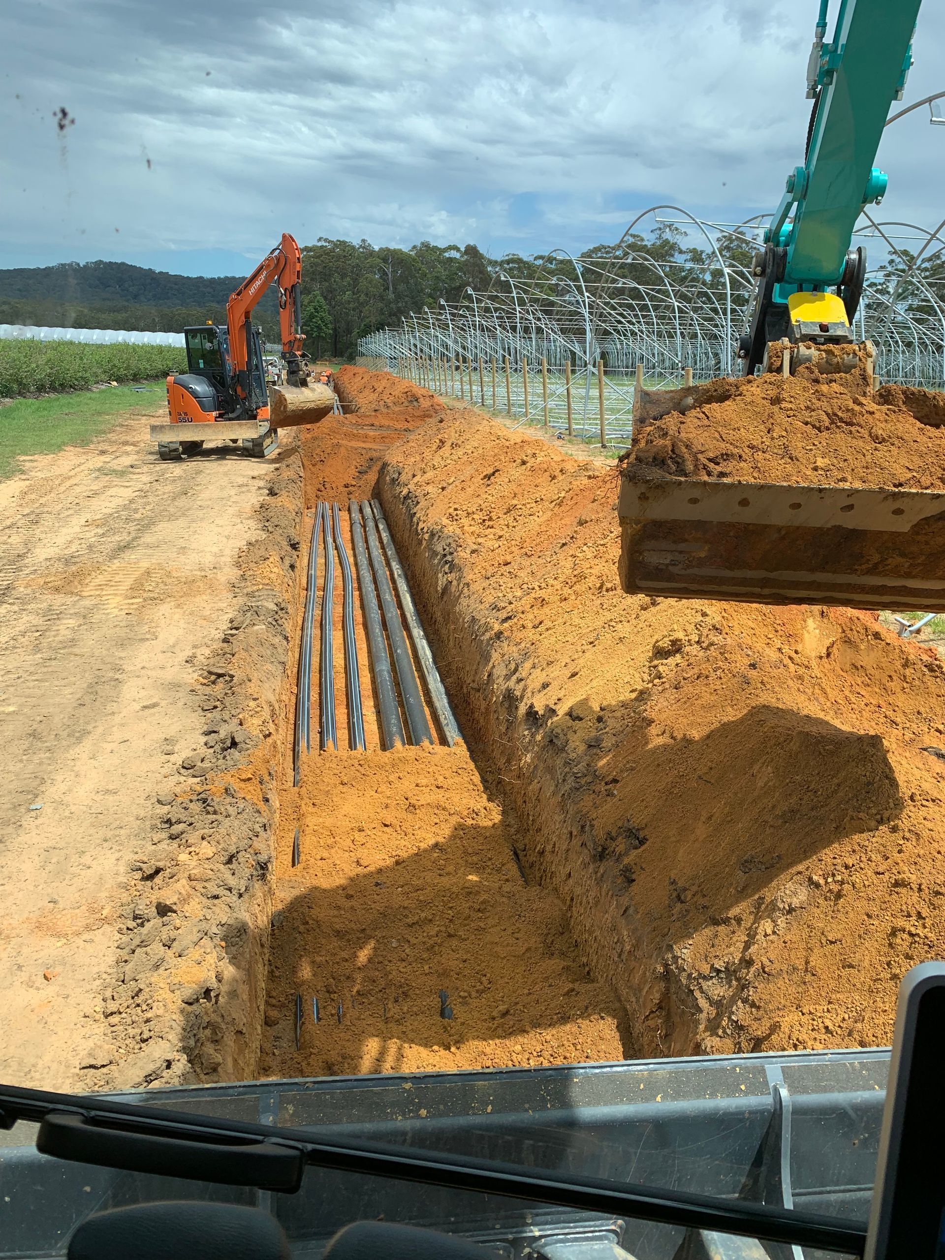 A pile of large metal pipes are being installed in a trench — Bennettron Demex in Corindi Beach, NSW