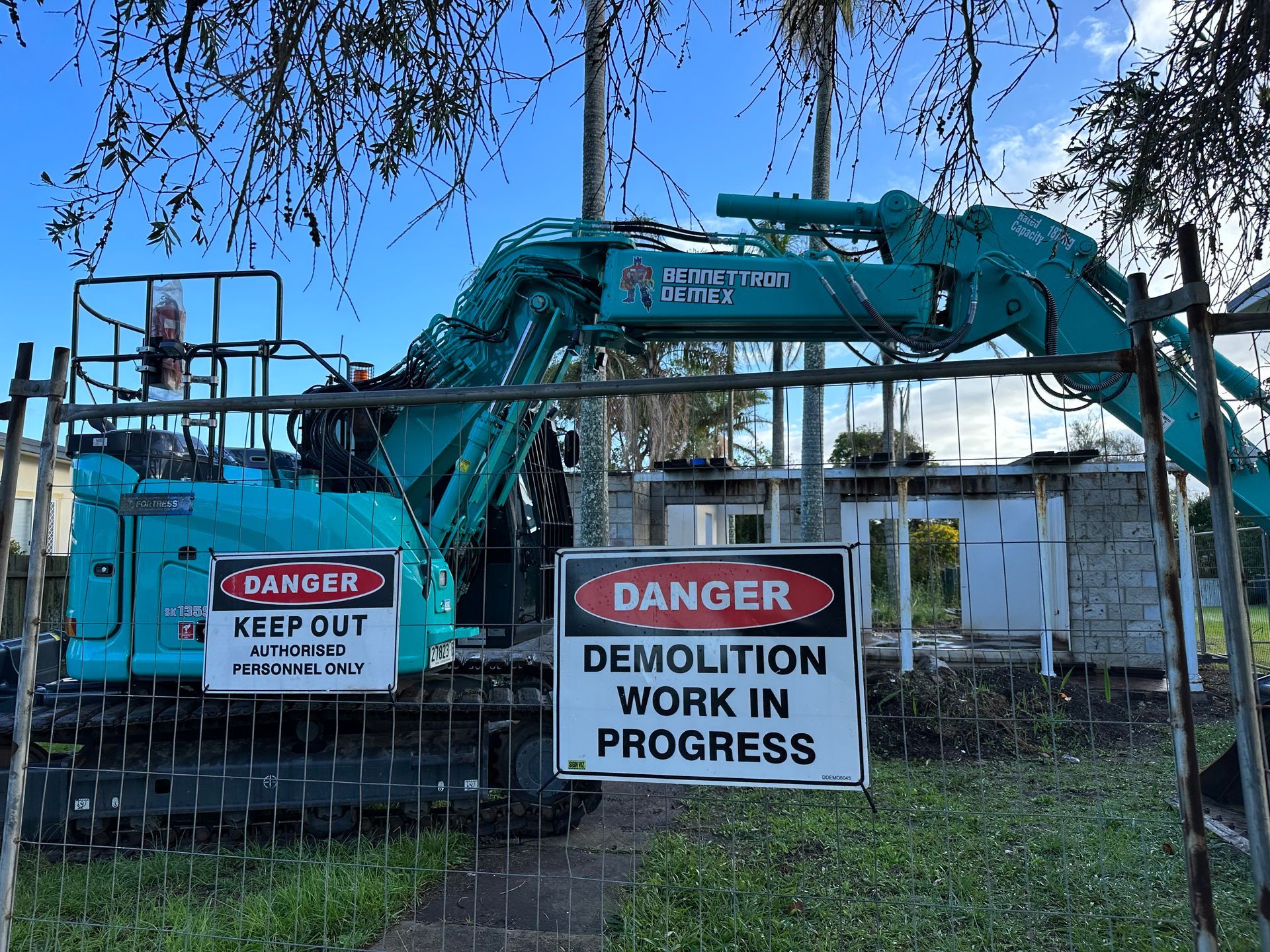 A Blue Excavator is Parked behind metal fence— Bennettron Demex in Corindi Beach, NSW