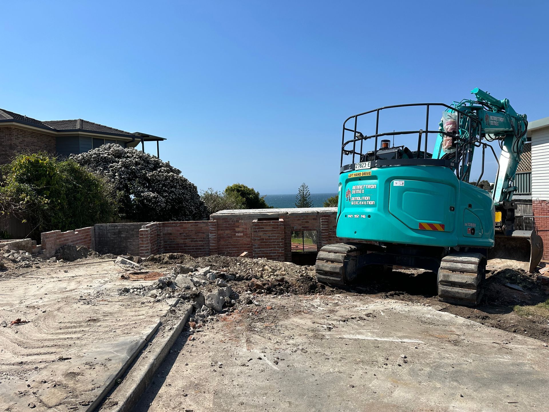 A large blue digger is looking out to ocean while on an empty lot of rock and rubble— Bennettron Demex in Corindi Beach, NSW