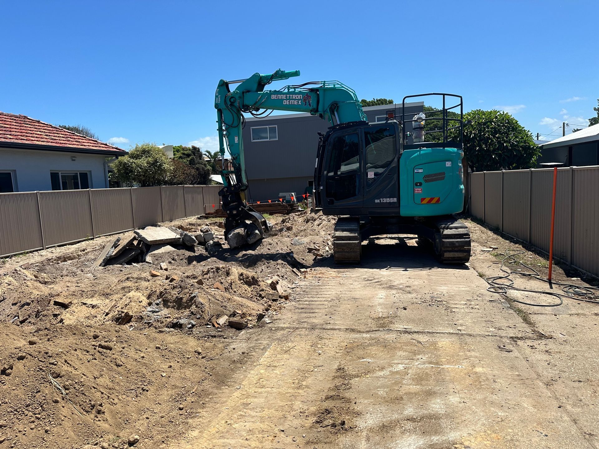 A large blue digger is moving a pile of dirt on empty lot — Bennettron Demex in Corindi Beach, NSW