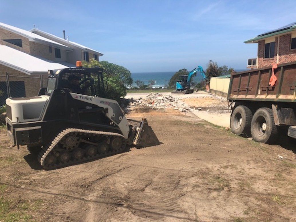 A Bulldozer is Driving Down a Dirt Road Next to a Dump Truck — Bennettron Demex in Sawtell, NSW