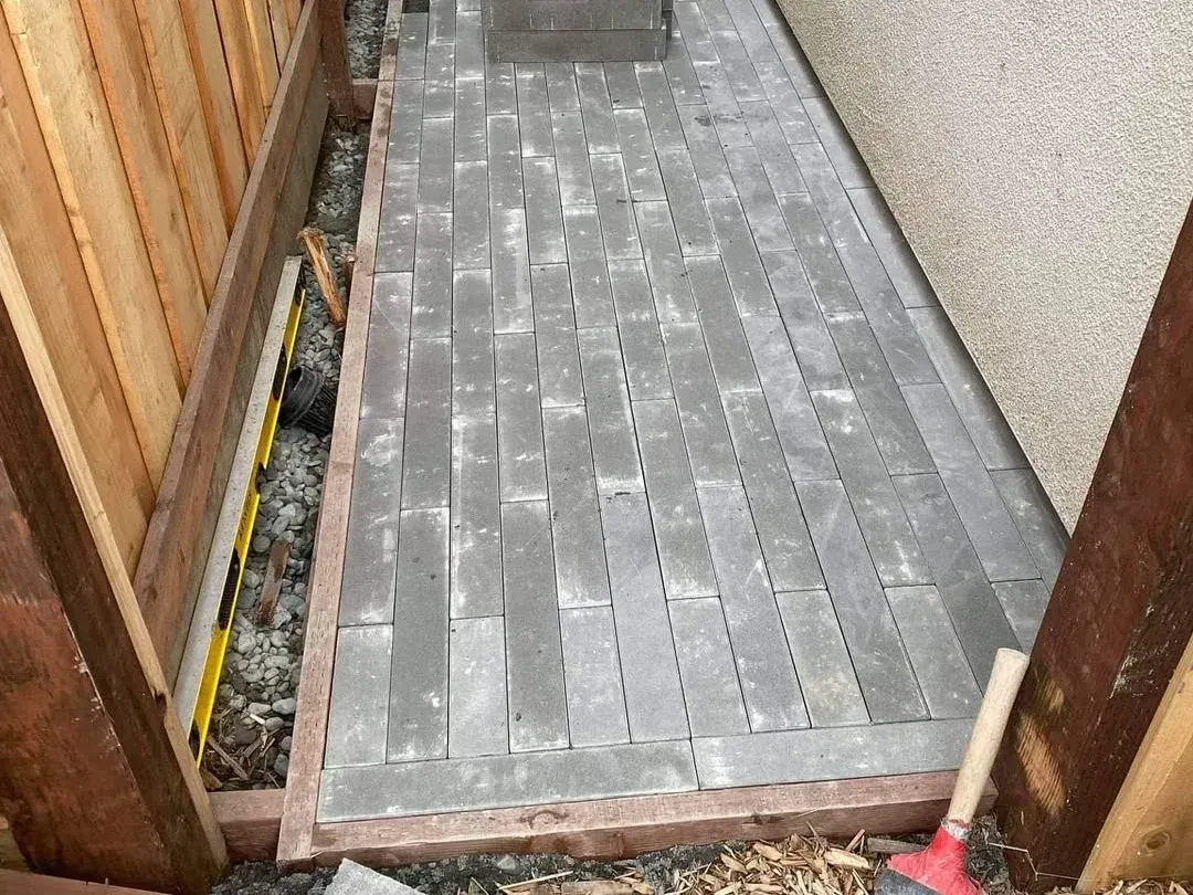 Narrow outdoor walkway with gray pavers between a wooden fence and a stucco wall