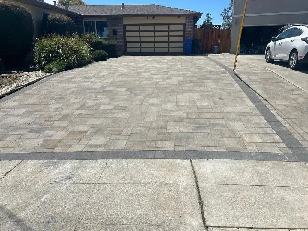 Wide paved driveway leading to a house with a garage, with a white car parked on the right.