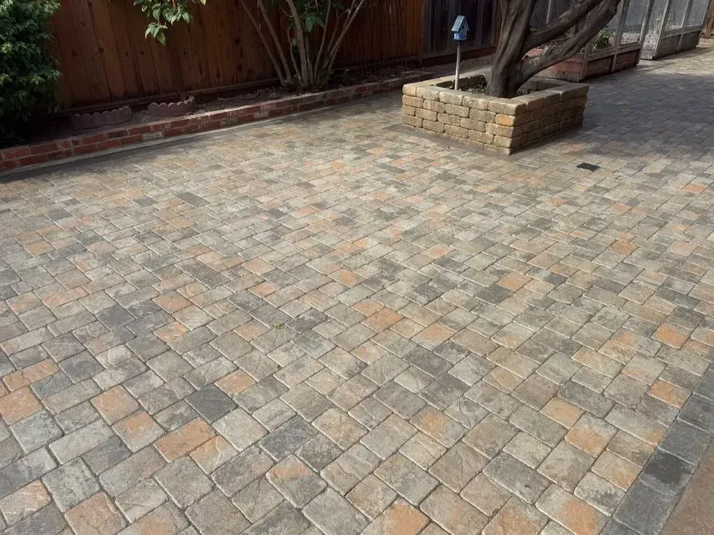 Brick-paved driveway with a small stone planter and fence in the background
