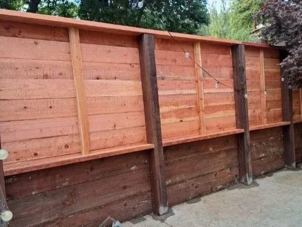 Wooden privacy fence with horizontal red-brown planks and dark support posts beside a concrete path.