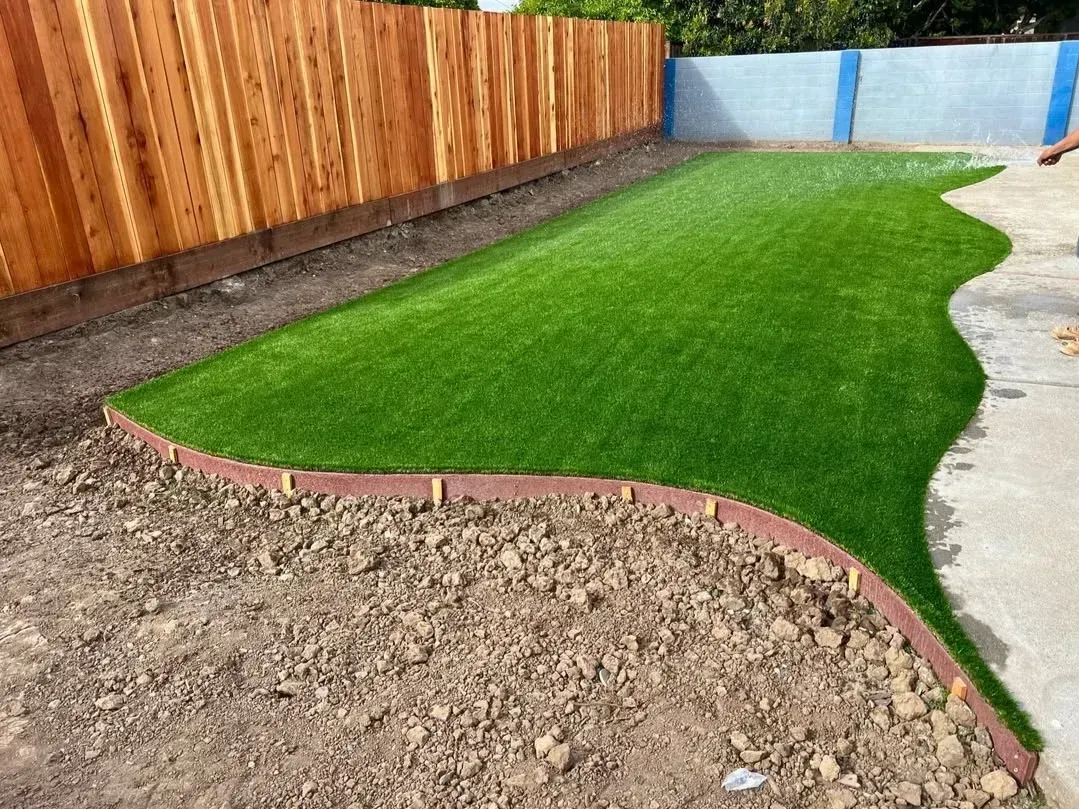 Freshly landscaped backyard with green lawn, curved brick edging, wooden fence, and concrete path.