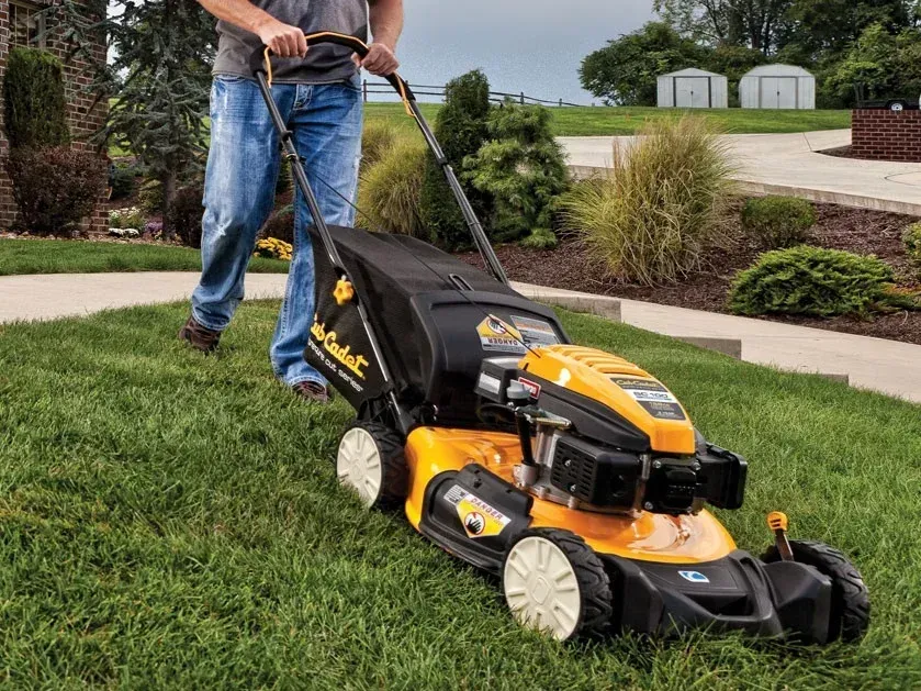Person pushing a yellow-and-black lawn mower across a grassy lawn.