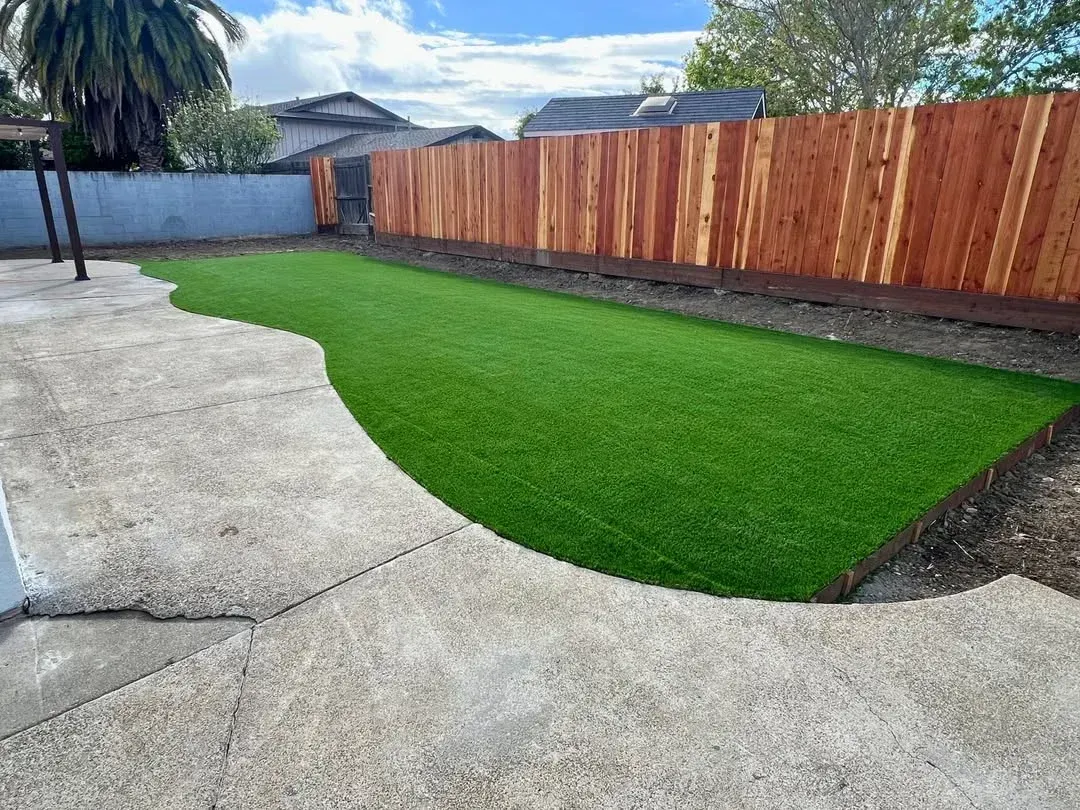Backyard with bright green lawn, concrete patio, and a red wooden fence along the side.
