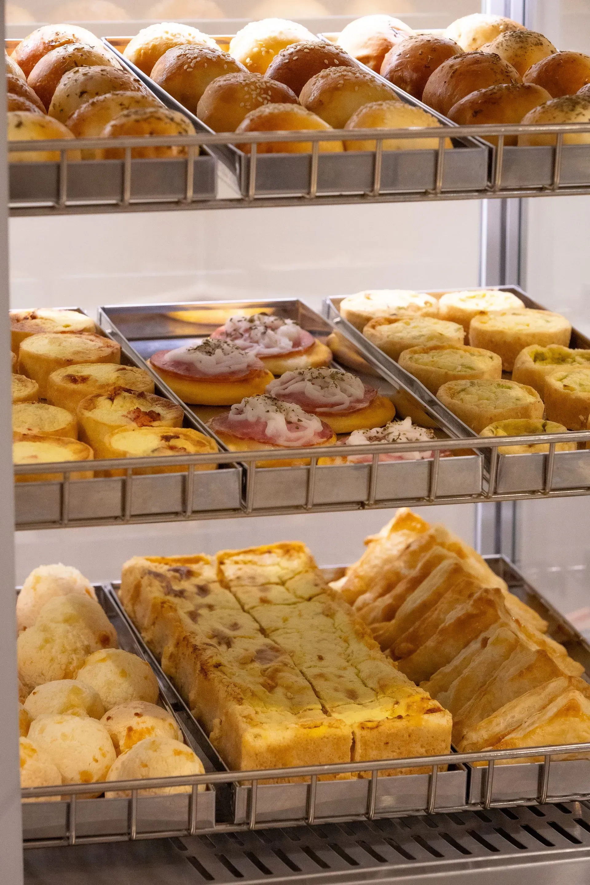 Vitrine de padaria com diversos pães e doces em bandejas de metal.