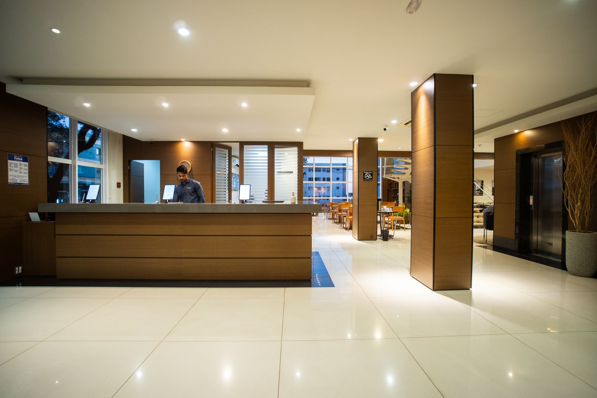 Área de refeições do restaurante com mesas e cadeiras de madeira, buffet e uma pequena TV na parede.