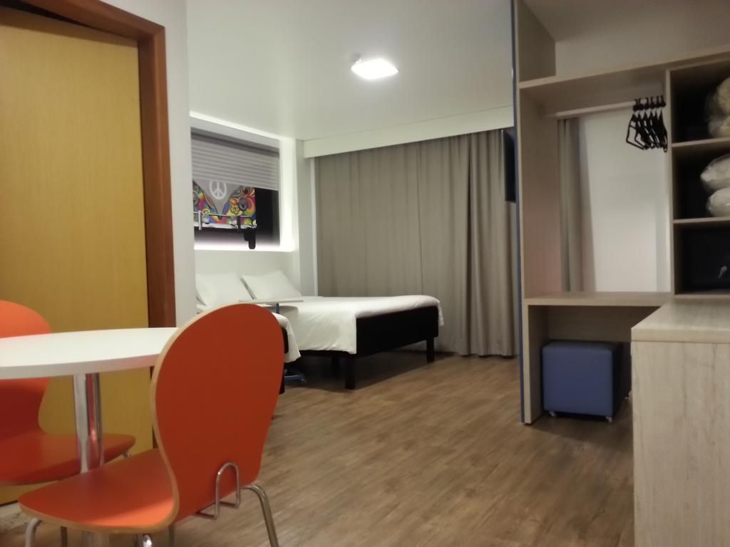 Quarto de hotel com cama, escrivaninha, obras de arte e piso de madeira.