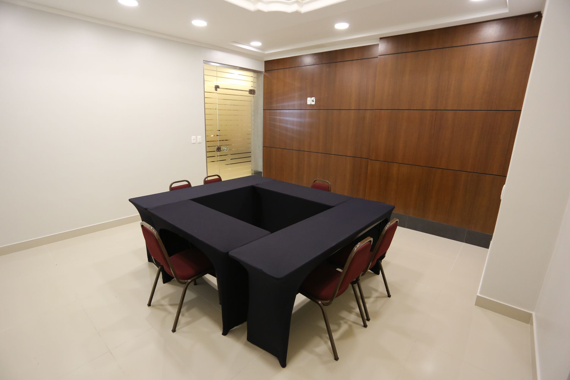 Sala de conferências com mesas e cadeiras azuis dispostas em forma de U.