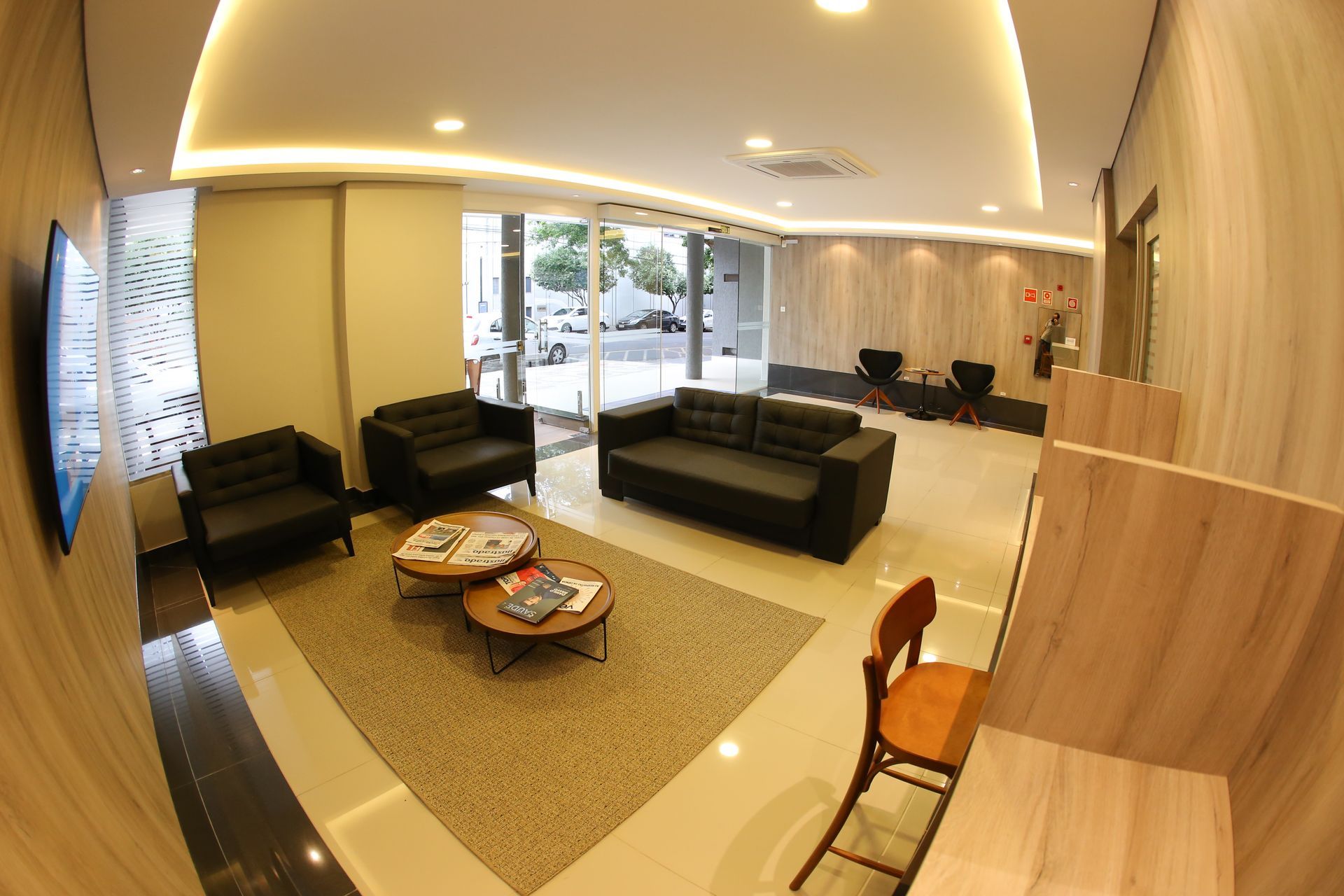 Área de recepção com balcão, paredes revestidas de madeira, sofá preto e iluminação suspensa.