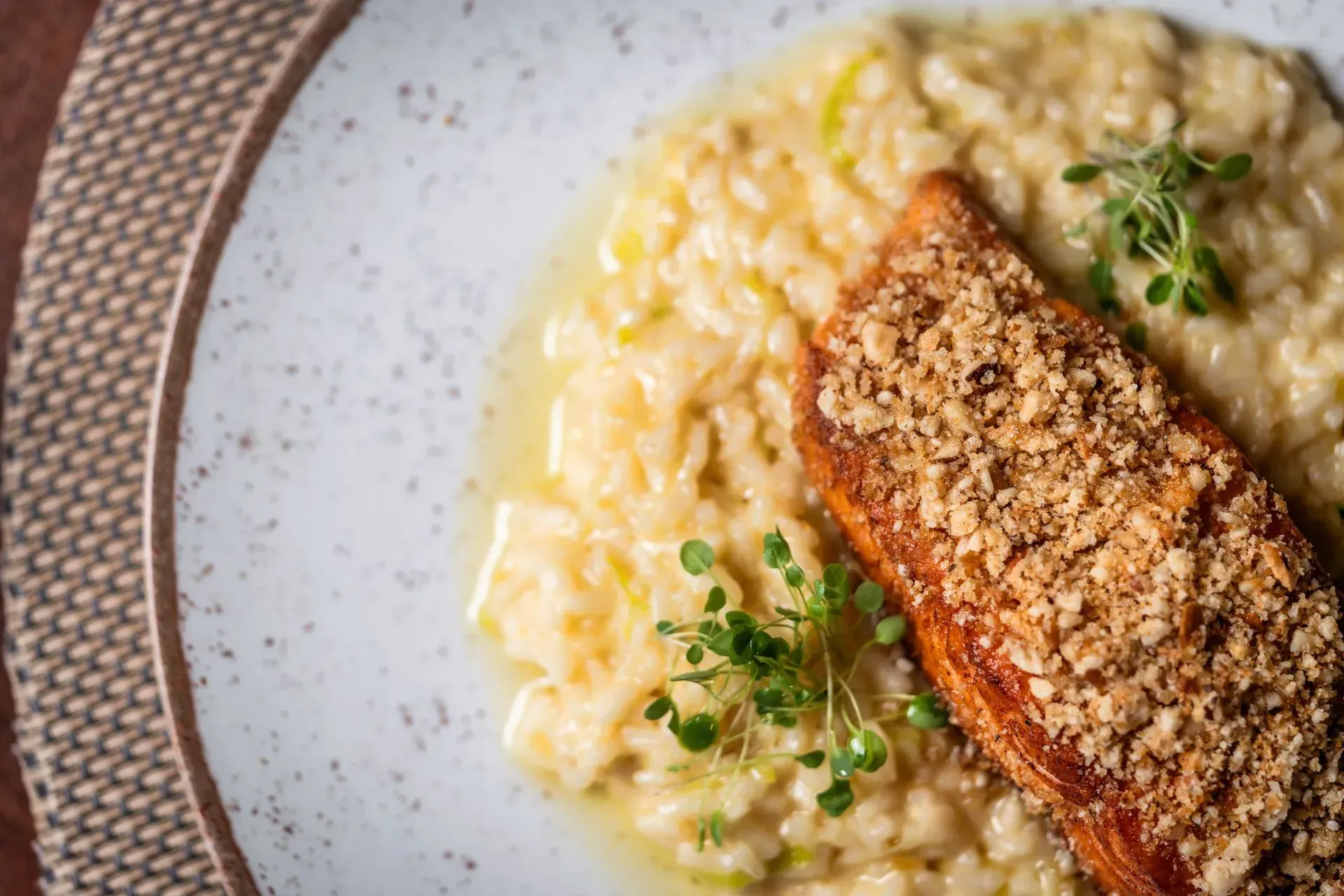 Salmão empanado com farinha de rosca e risoto em um prato claro, decorado com ervas.