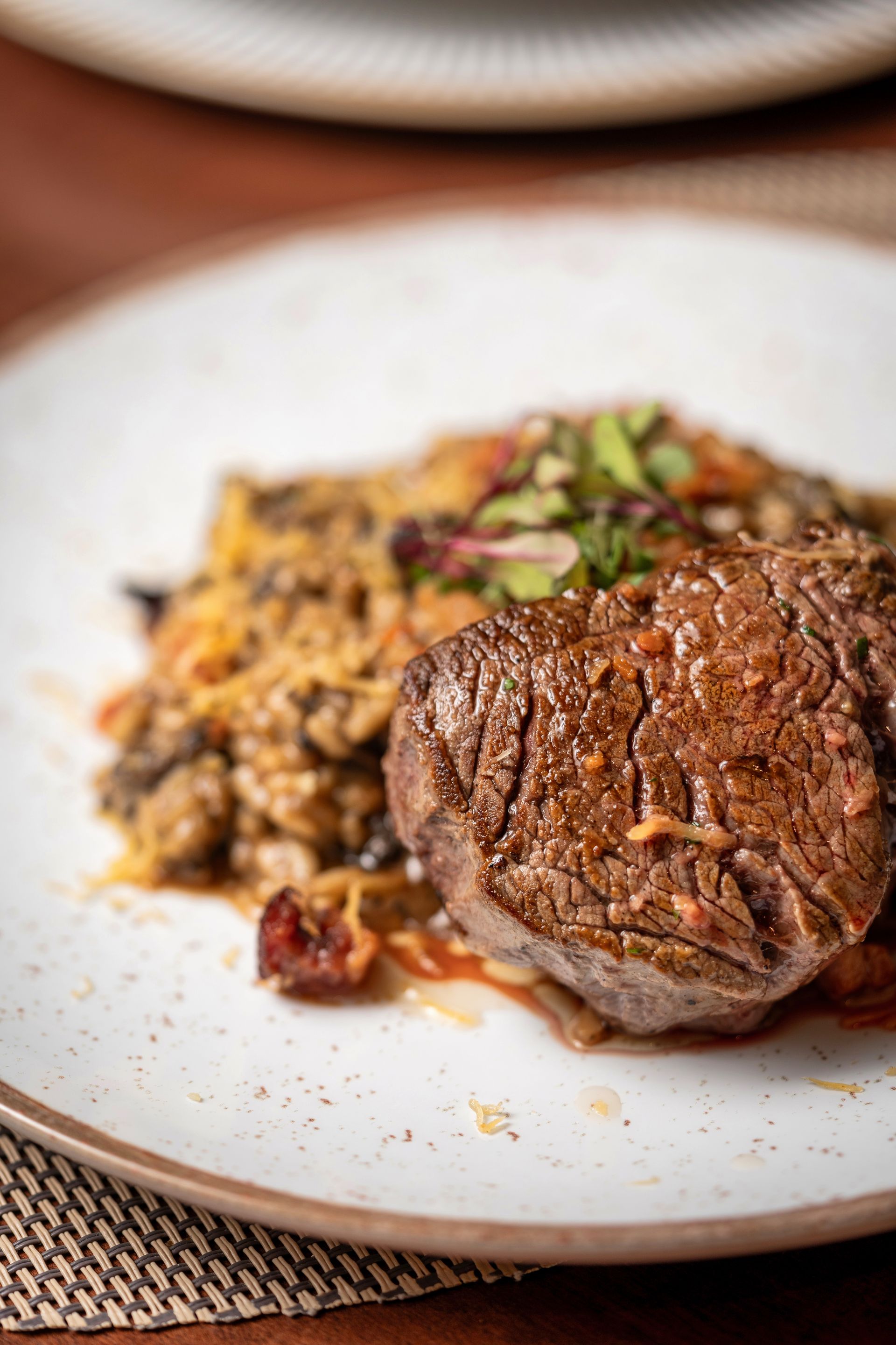 Close-up de um bife grelhado com acompanhamento de legumes temperados em um prato branco.