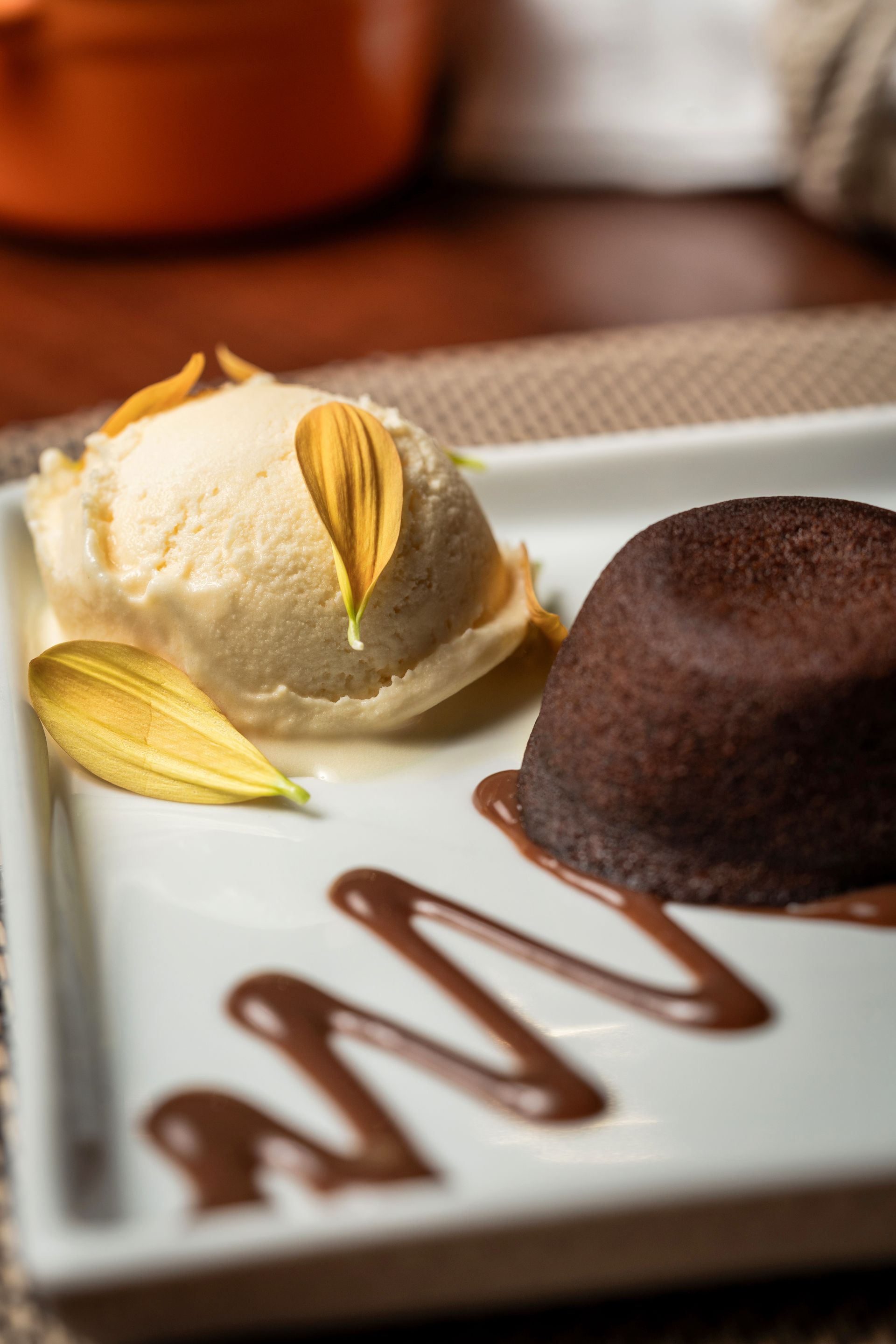 Bolo vulcão de chocolate com sorvete de baunilha e calda de chocolate servido em um prato branco.