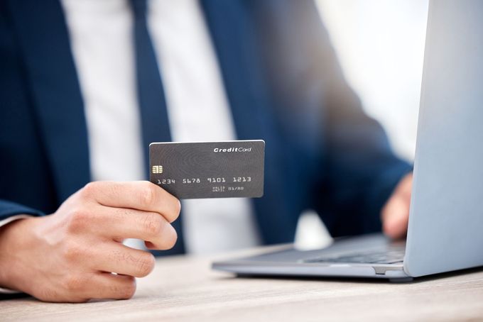 Man in a suit holding a black credit card near a laptop, possibly entering payment information.