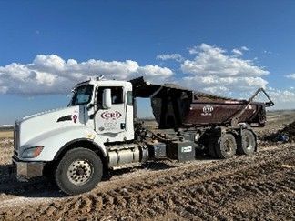 A roll-off truck delivering a dumpster on a dirt construction site. A roll-off truck delivering a dumpster on a dirt construction site.