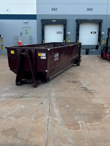 An dumpster placed on a concrete loading dock area in front of two white loading bay doors. An dumpster placed on a concrete loading dock area in front of two white loading bay doors.