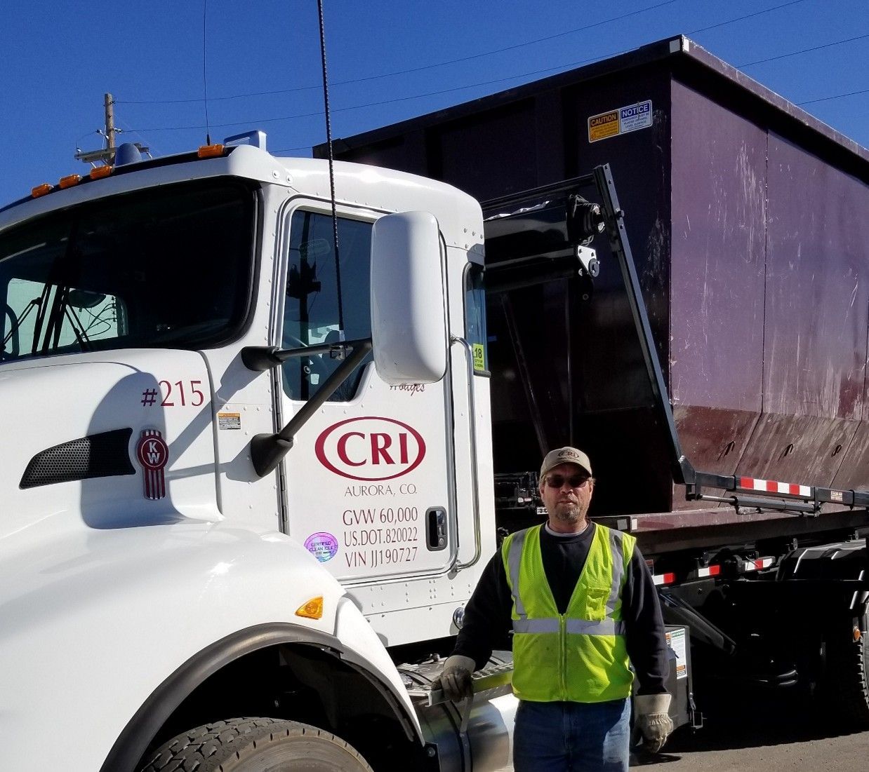 Worker standing beside a roll-off truck delivering a large commercial dumpster. Worker standing beside a roll-off truck delivering a large commercial dumpster.
