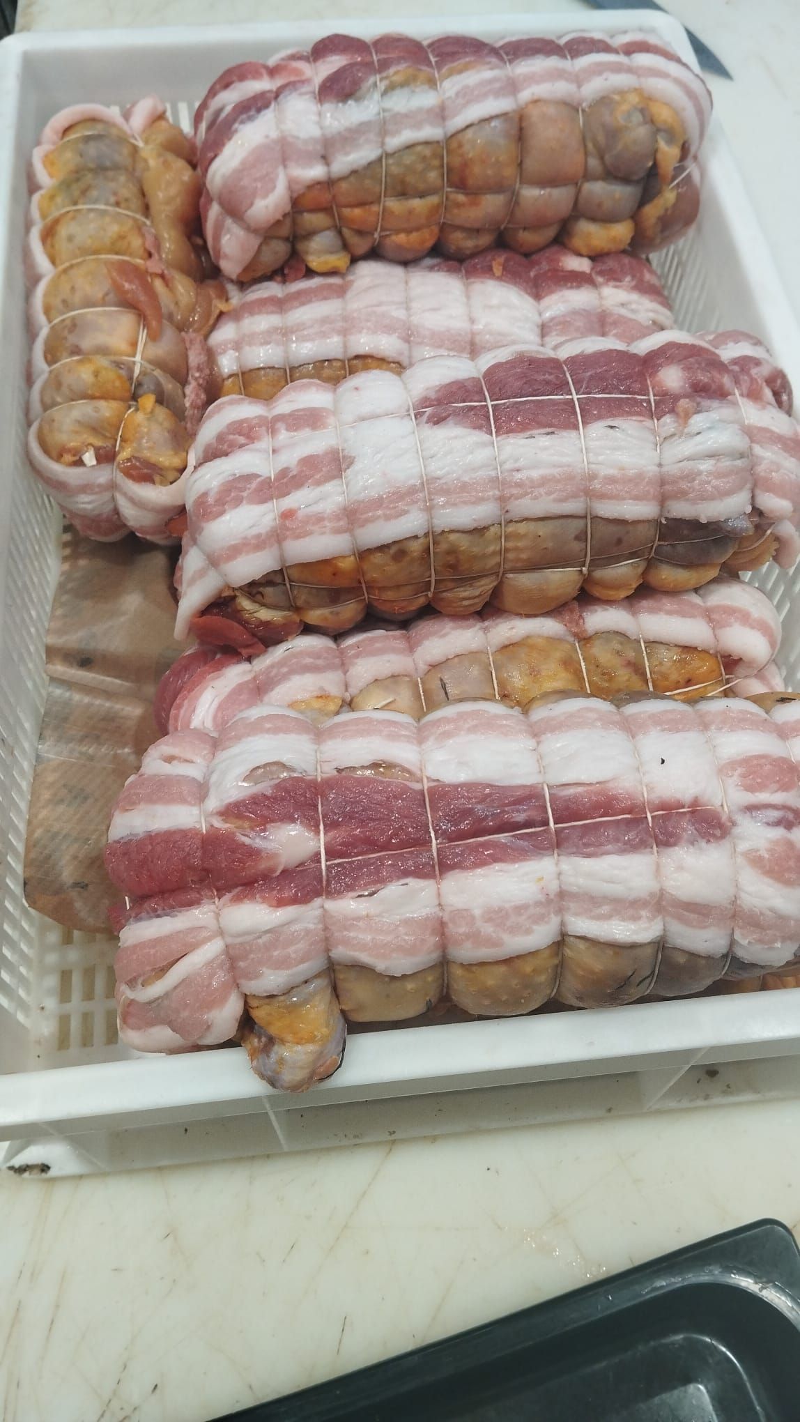 Vassoio di polpette di carne avvolte nella pancetta, legate con lo spago, pronte per la cottura.