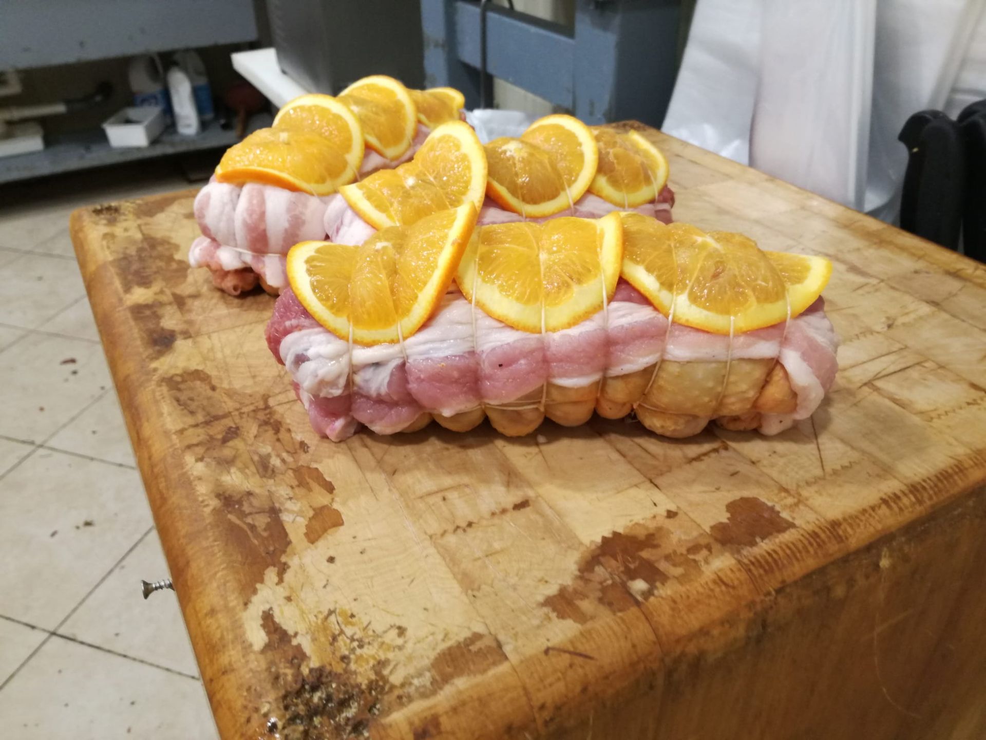 Due arrosti di maiale avvolti nella pancetta, guarnite con fette d'arancia, su un tagliere di legno.