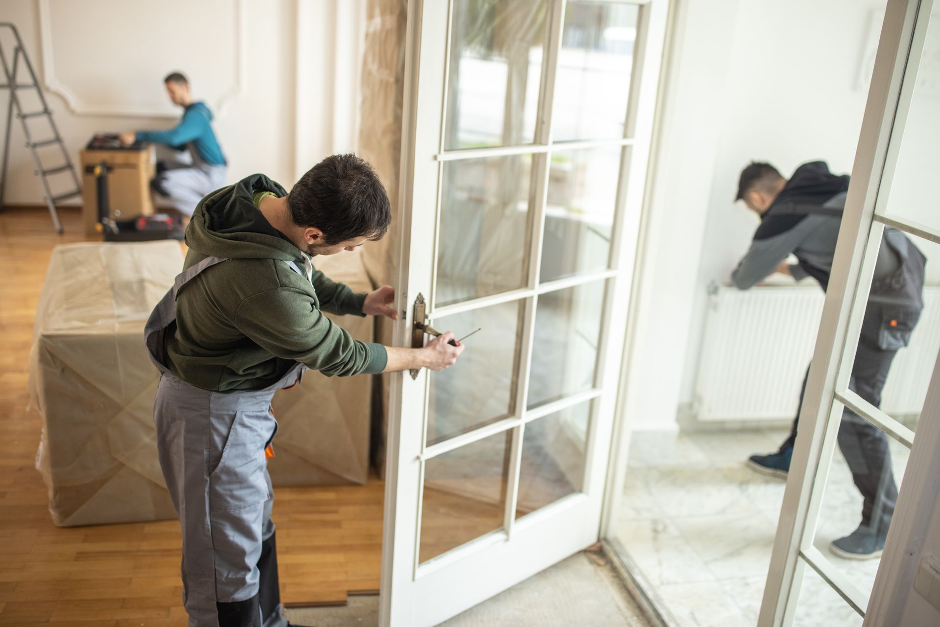 A man adjusts a door lock in a room, performing locksmith services to improve its functionality.