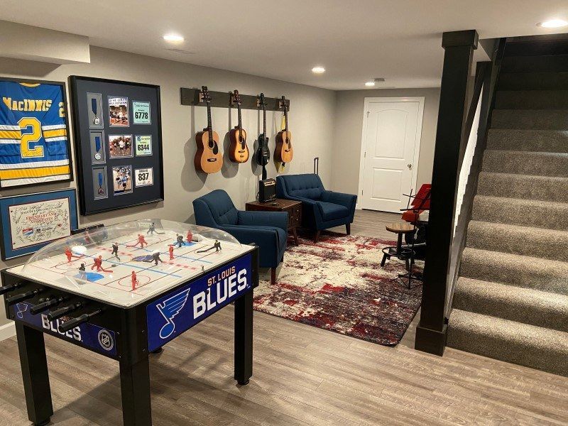 a basement with a foosball table , chairs , stairs and guitars hanging on the wall .