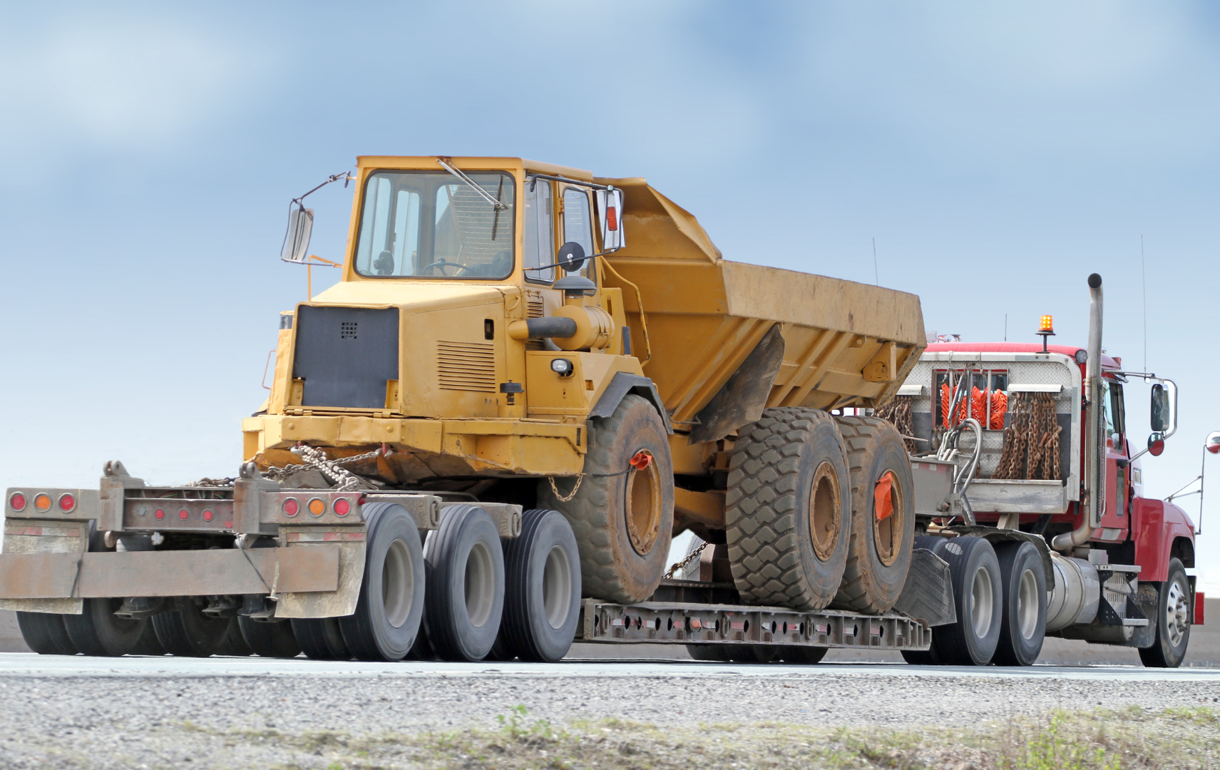 A large yellow dump truck is being hauled by a semi truck