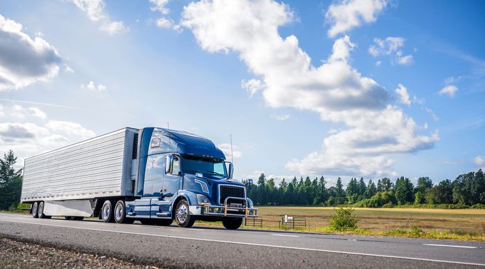 A blue semi truck is driving down a highway next to a field - transportation services