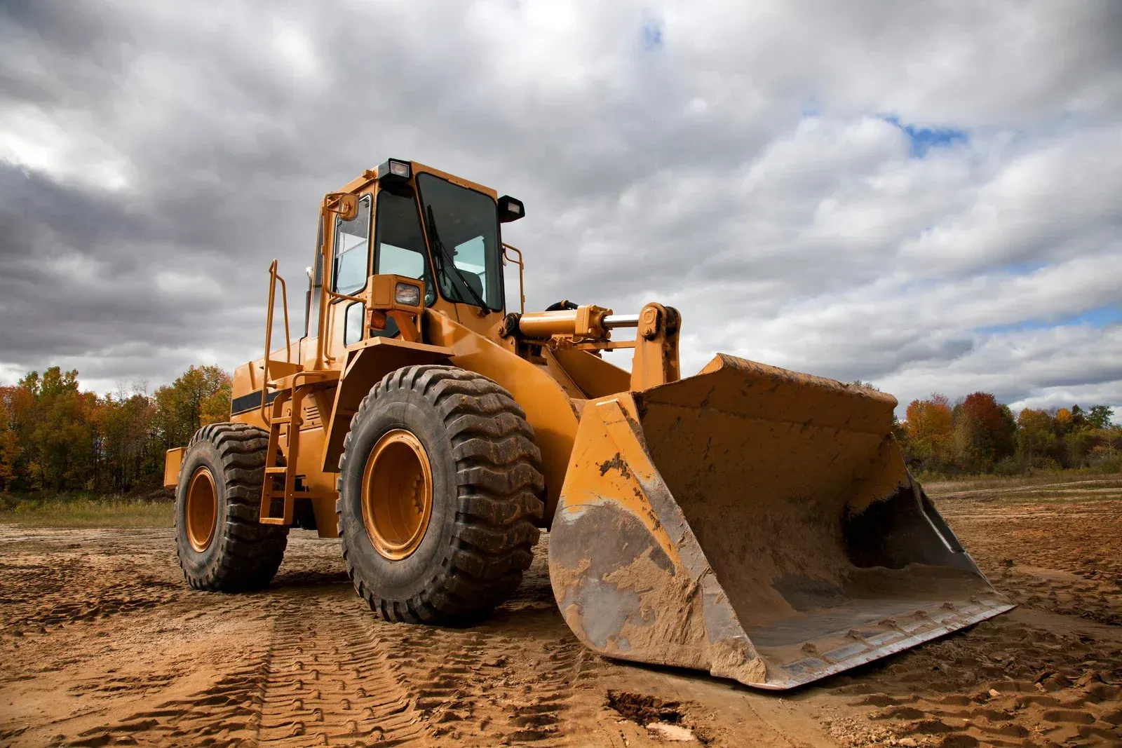 A yellow bulldozer with a large bucket is parked in a dirt field.