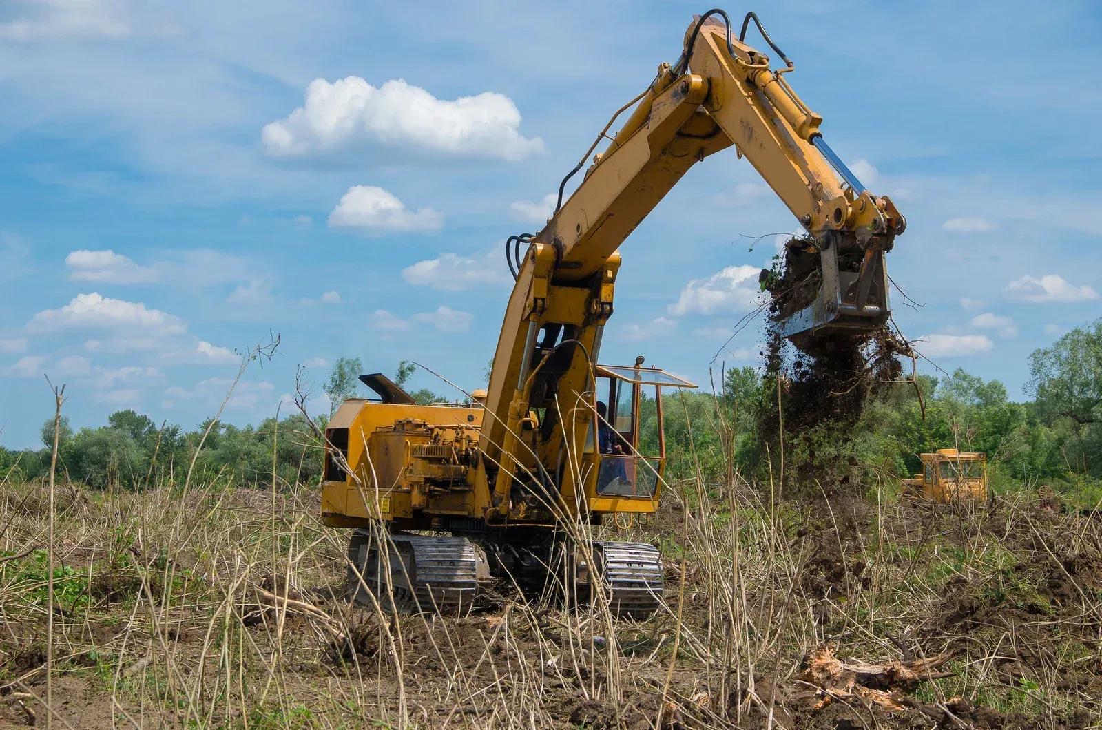 A yellow excavator is moving dirt in a field.
