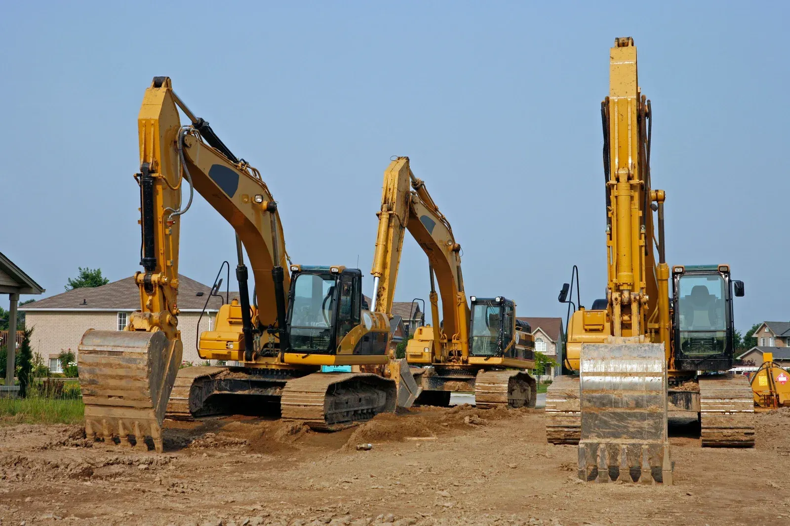 Three yellow excavators are lined up in a dirt field.