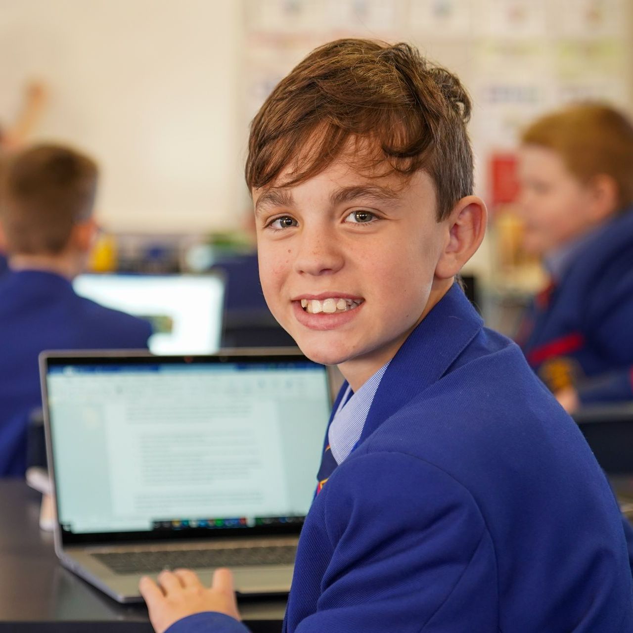 Student looking back from his laptop smiling.