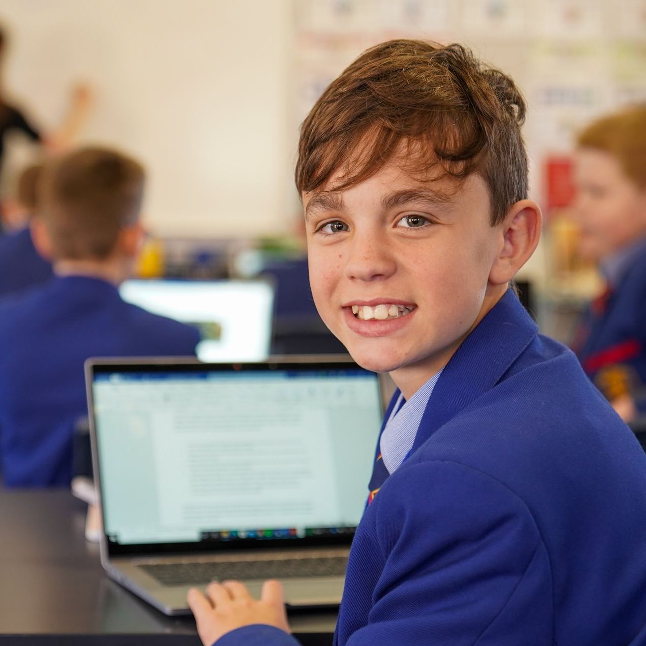 Student looking back from his laptop smiling.