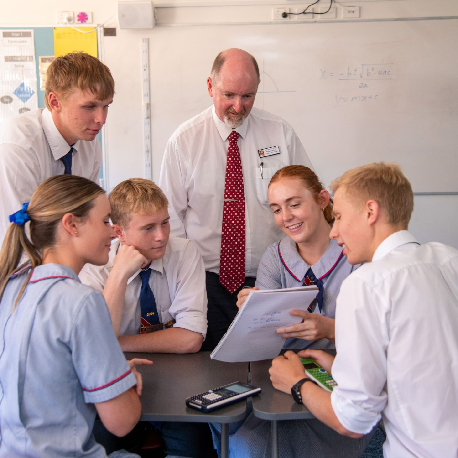 Senior School students in mathematics class crowded around a table with the teacher assisting in the background.