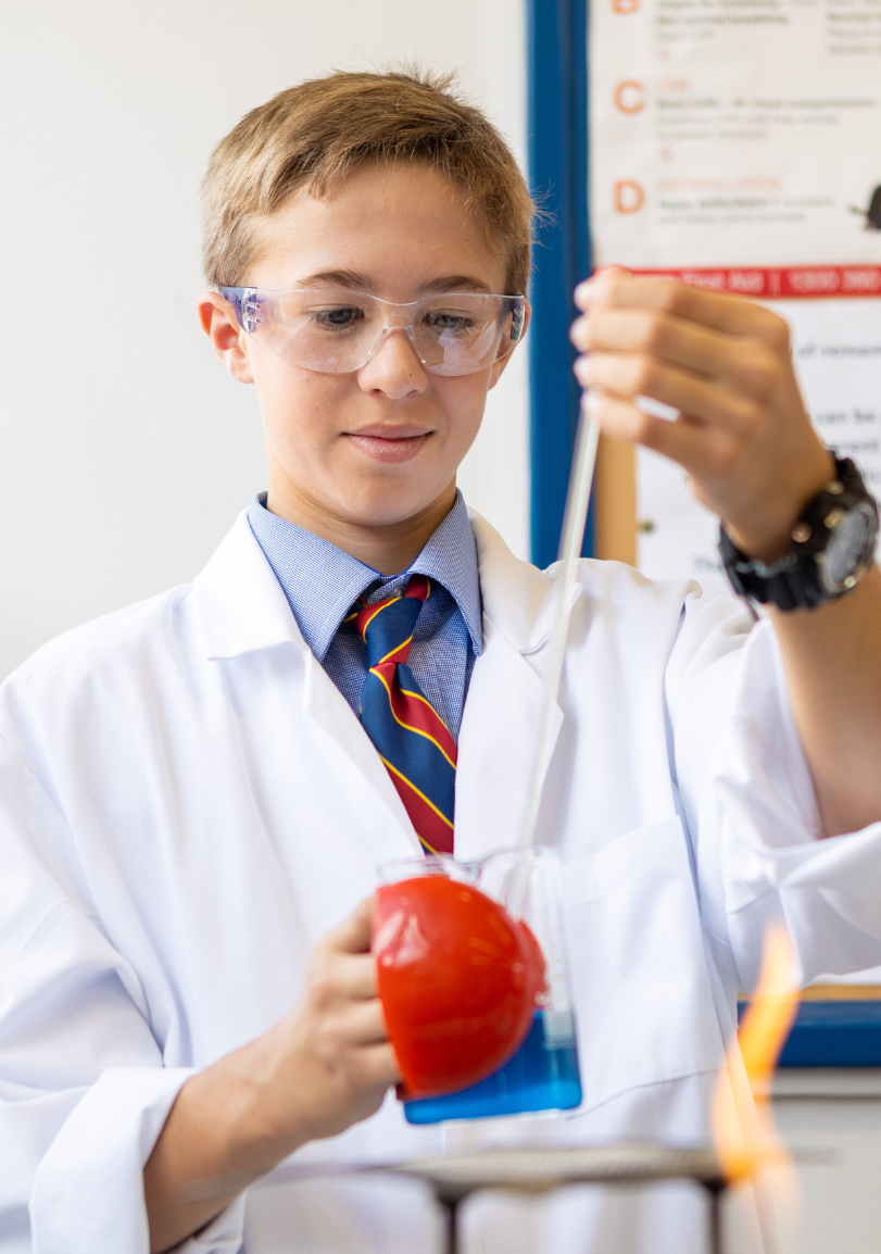 A school boy in a lab coat is holding a beaker and a tomato.