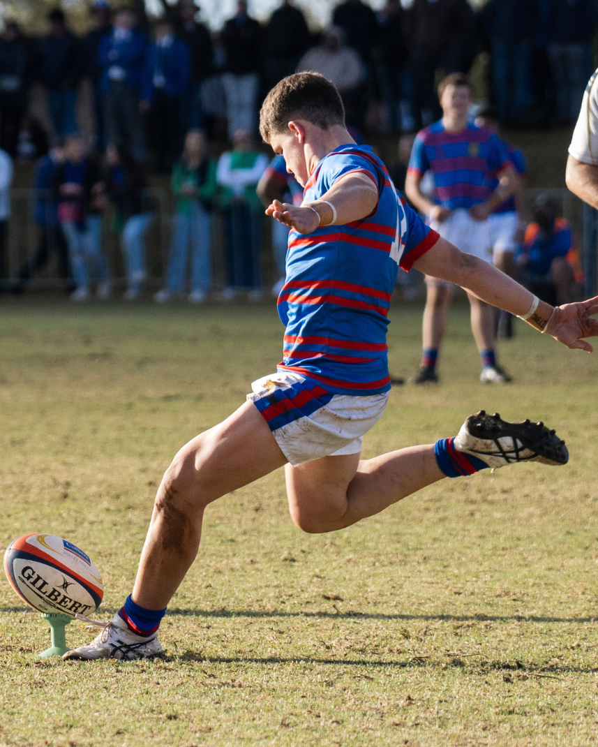 A student is kicking a rugby ball on a field.