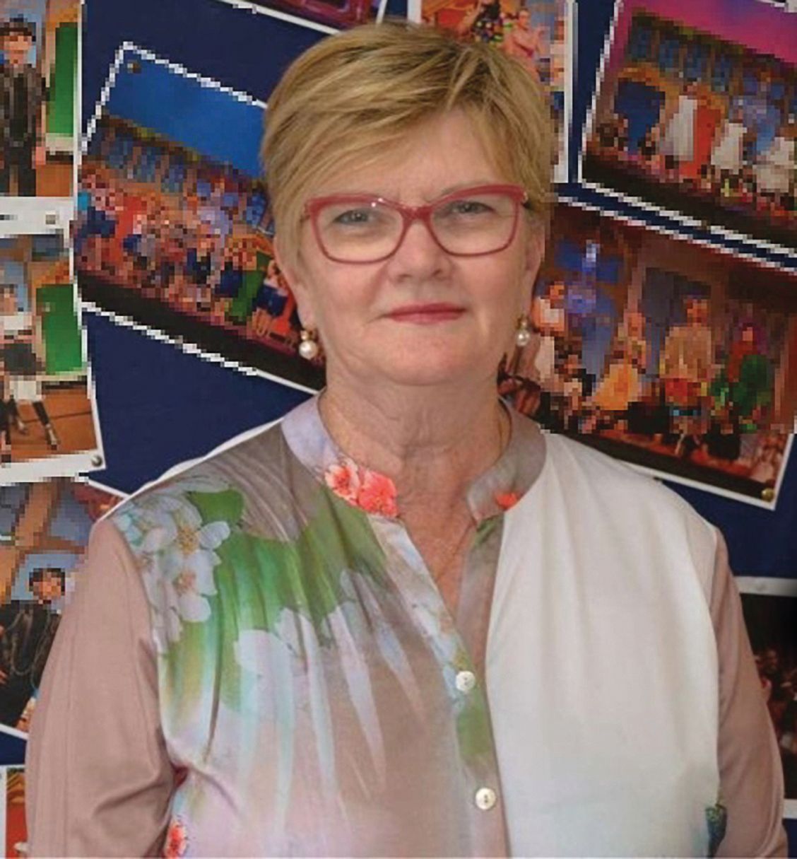 A woman wearing glasses and a black jacket is standing in front of a bush.