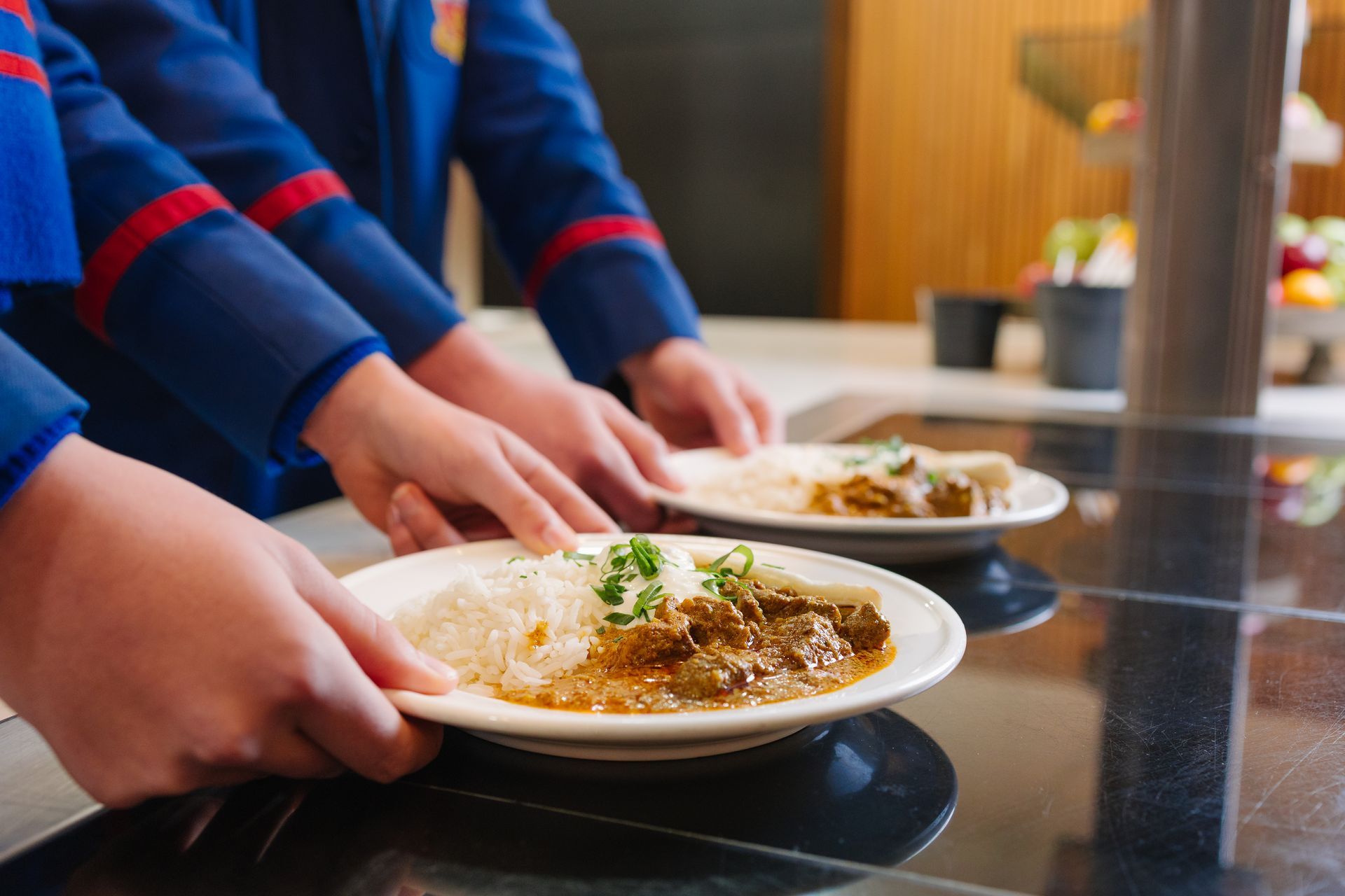 Student hands holding a curry and rice dish for a meal.