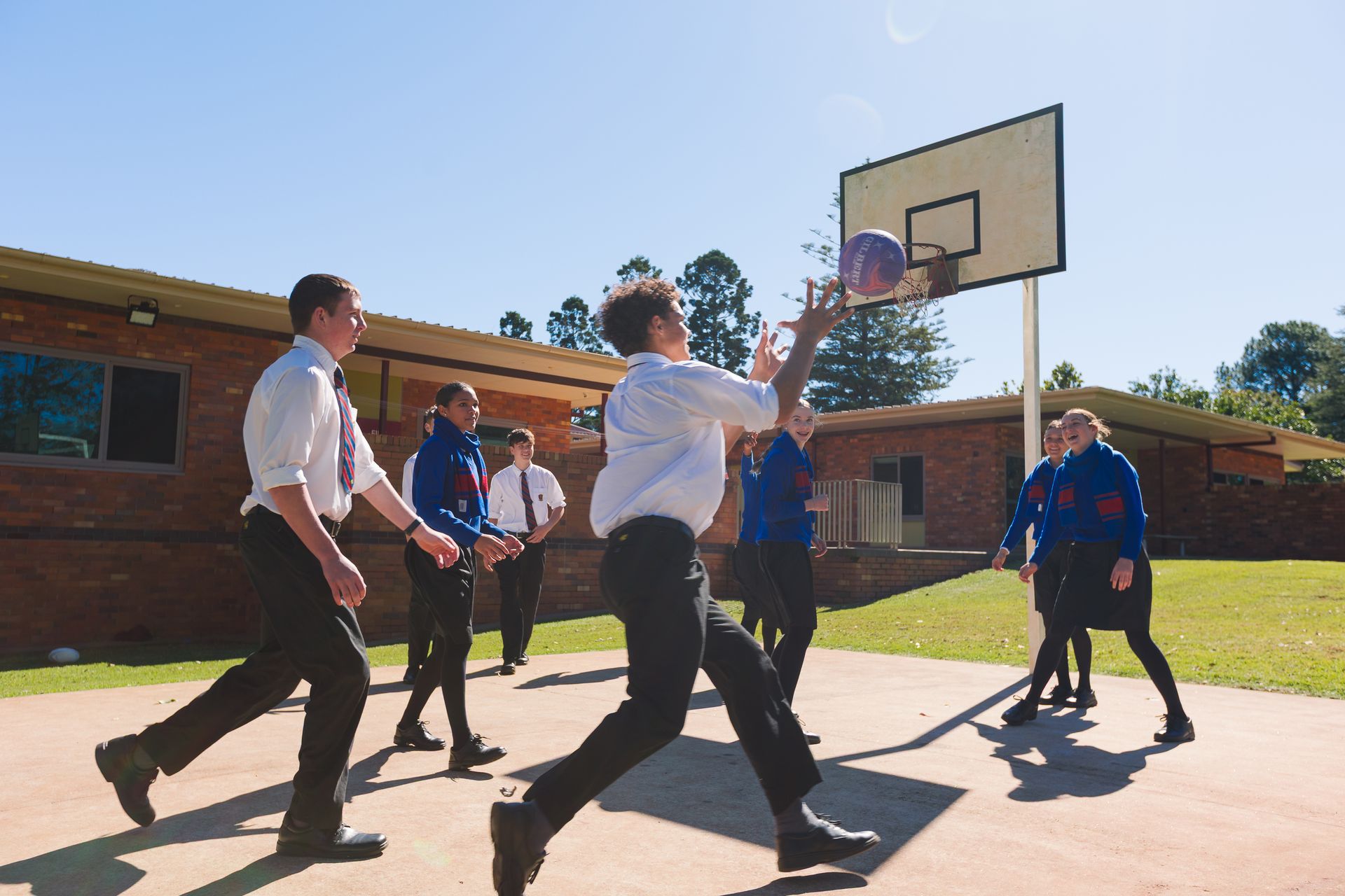 Seven boarding student playing basketball, with one student shooting a basketball at a hoop, with the ball in mid-air. 