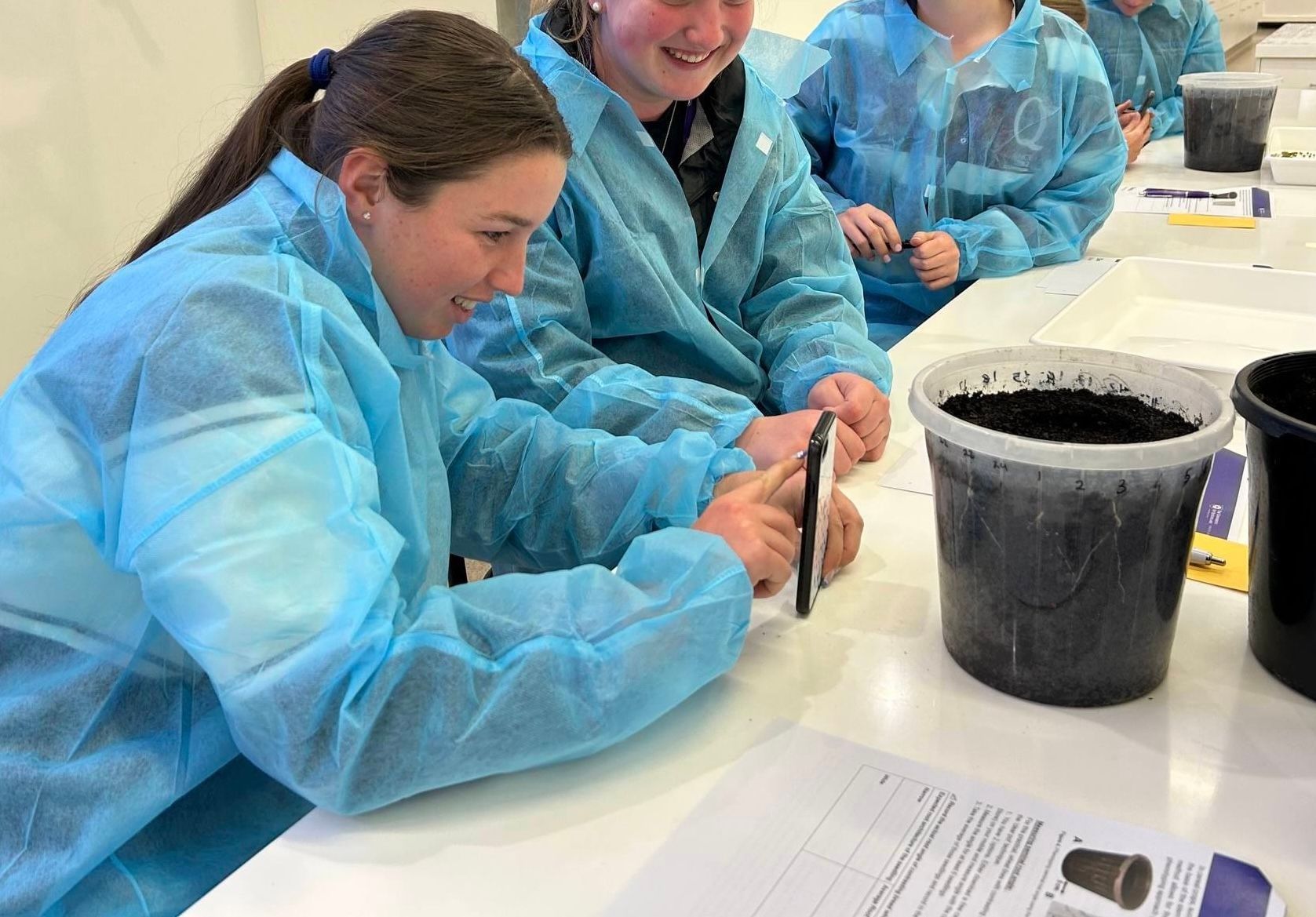 Downlands student in a blue lab coat photographing soil