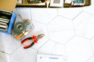 Pliers, a roll of tape, and tool boxes sit on a white, marble-patterned hexagonal tile floor.