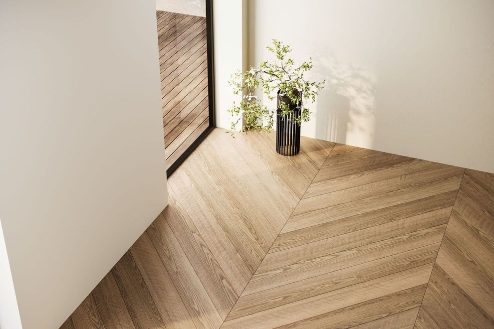 A light-colored wooden floor with a chevron pattern next to a white wall and a plant in a black vase.