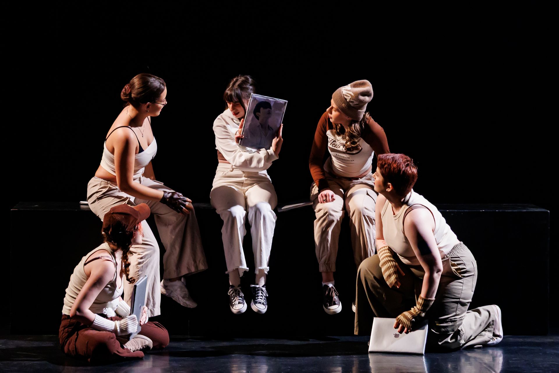 Cinco pessoas. Uma pessoa segura uma fotografia, enquanto as outras observam.