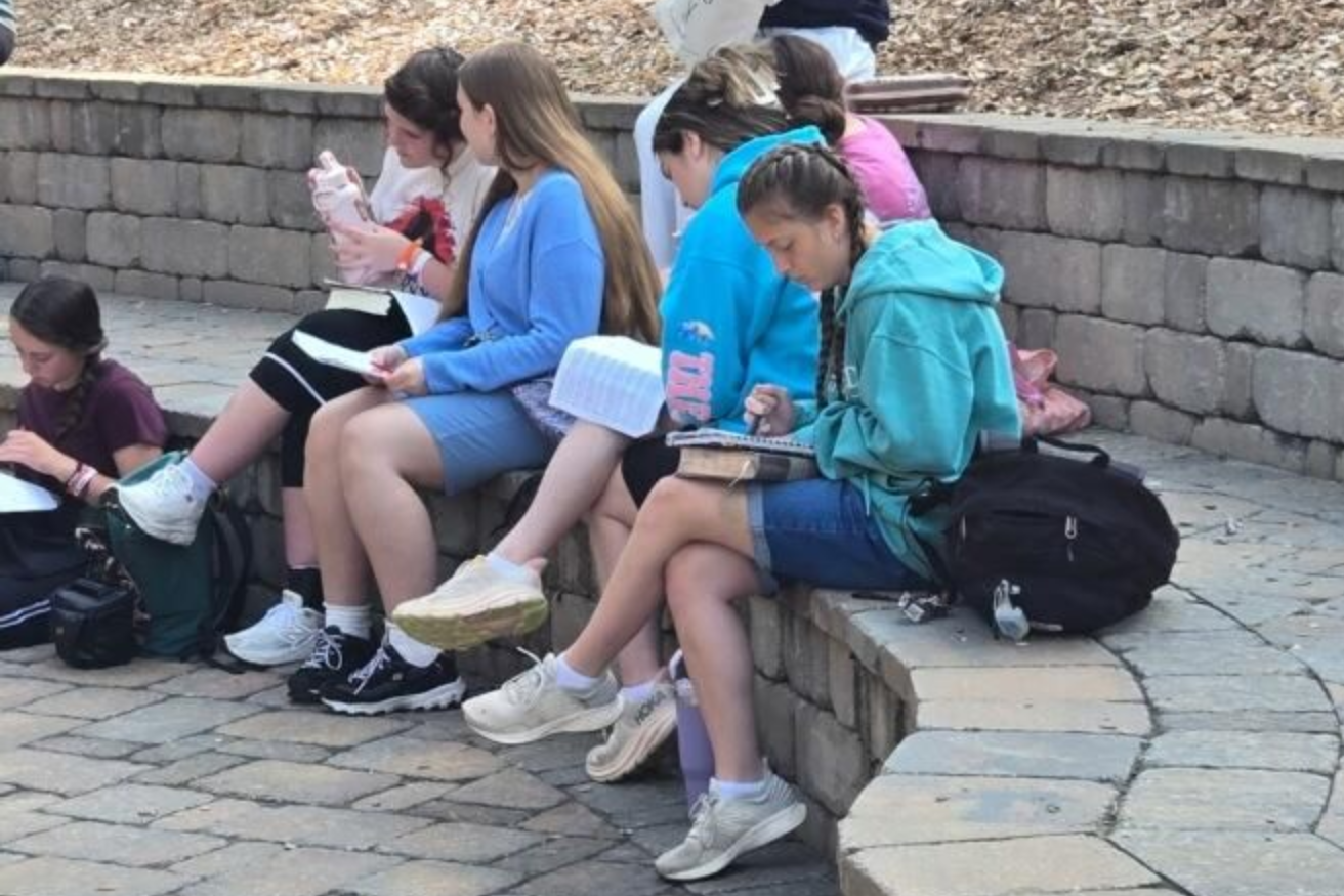 A group of students sitting on a stone wall outdoors, studying and looking at notebooks.