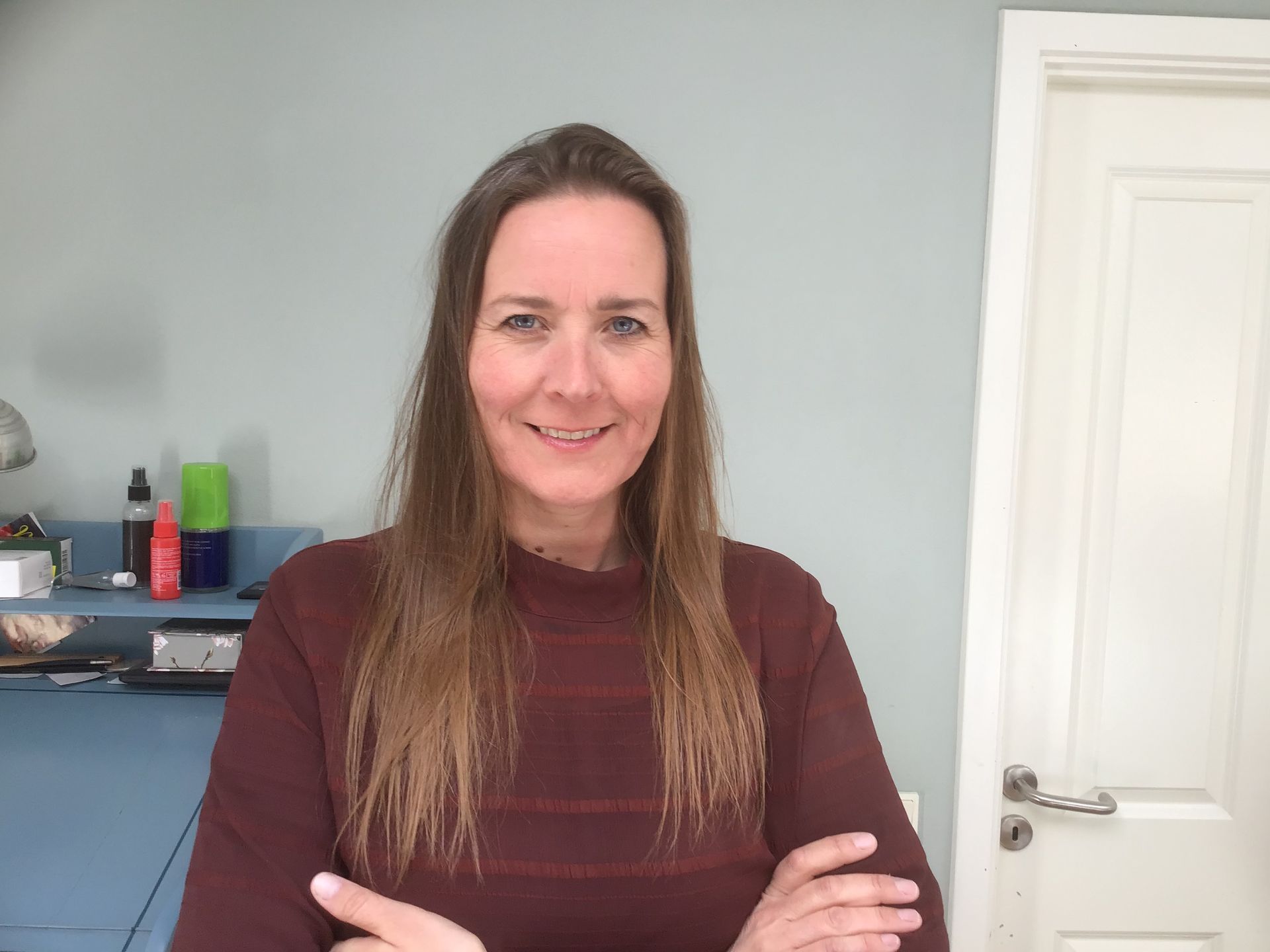 En kvinde står foran en dør med armene over kors og smiler.